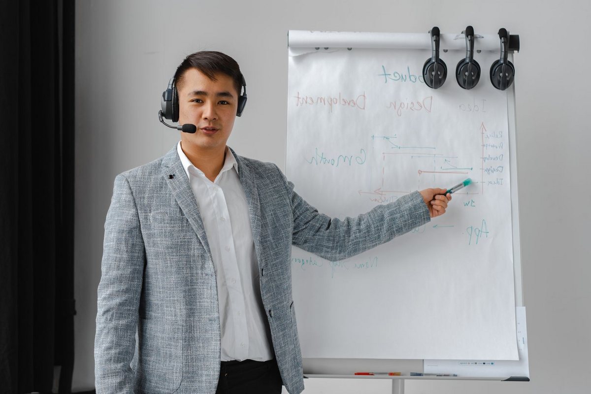 A trainer wearing a headset presenting a delivery plan on a flip chart